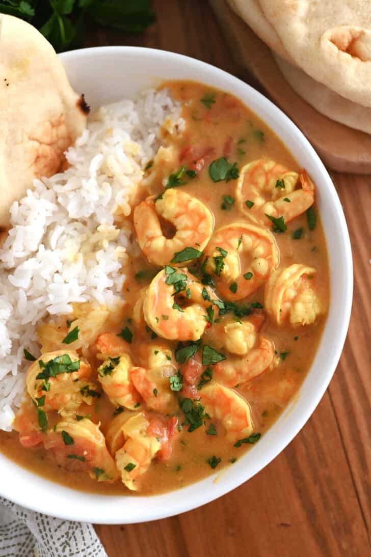 Top down view of a white bowl with flatbread, white rice, and shrimp in a curry sauce.