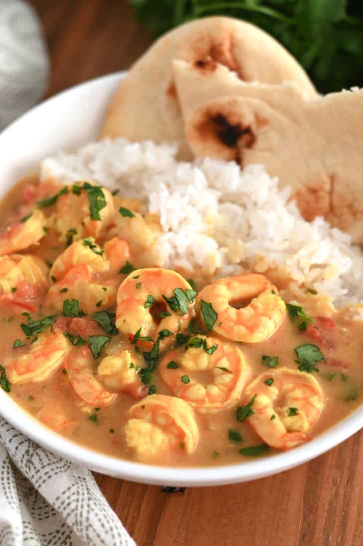 A white bowl with flatbread, white rice, and shrimp in a curry sauce.