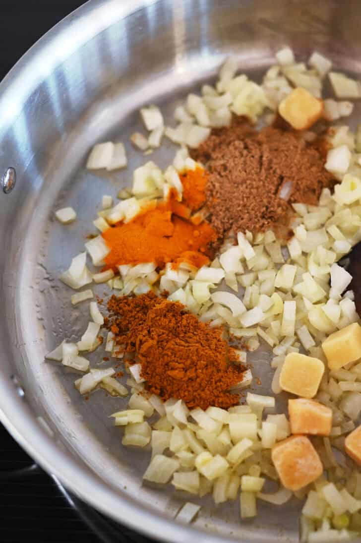 Top down view of a metal pot with diced onions and curry spices.
