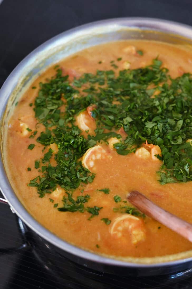 Top down view of a shrimp curry in a metal pot with chopped parsley on top.