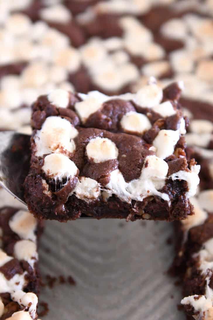One chocolate cookie bar with pecans and marshmallows on square spatula over pan of bars.
