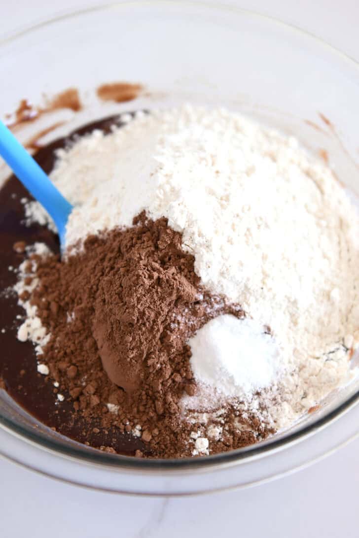 Glass bowl with cocoa powder and flour on top of melted chocolate mixture.