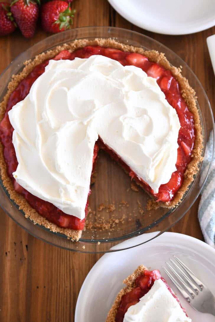 Strawberry pie with whipped cream on top with slice cut and taken out.