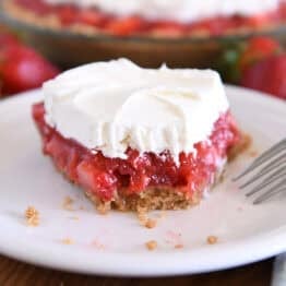 Half eaten slice of strawberry pie with whipped cream on top on white plate.