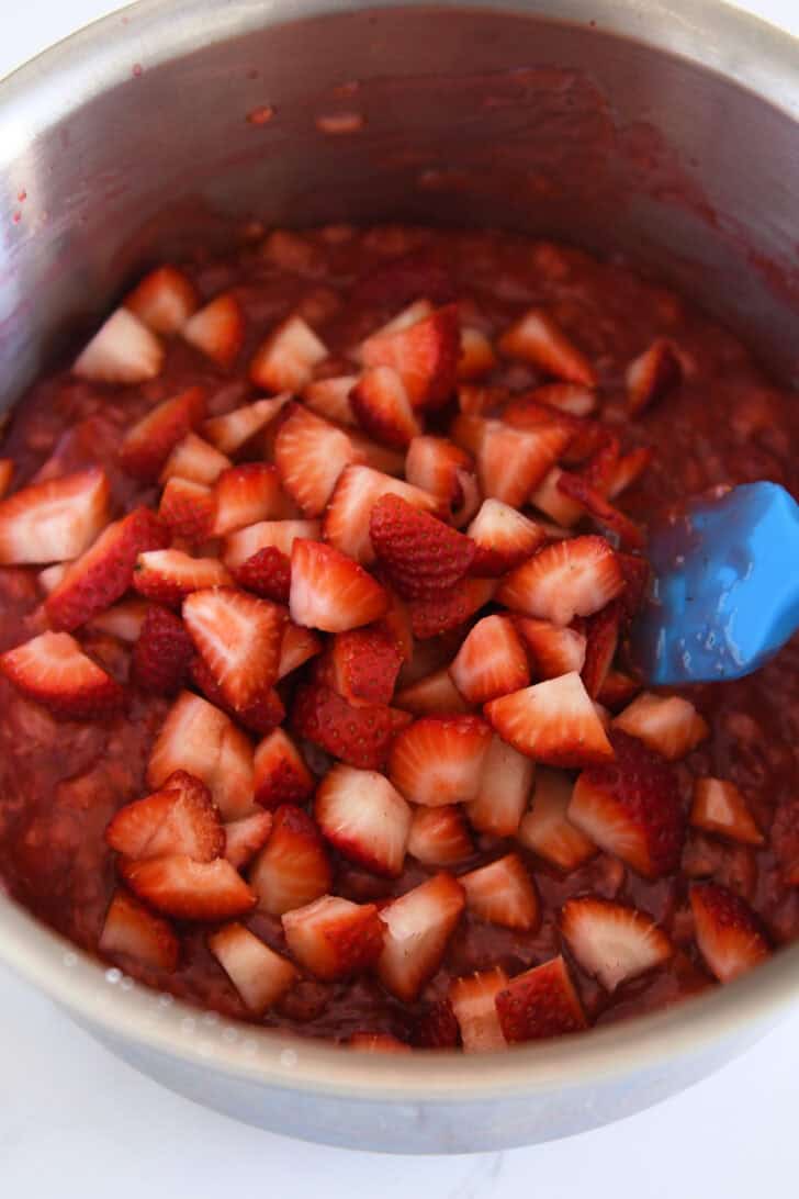 Fresh strawberries added to thick strawberry mixture in stainless pot.