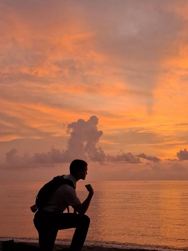 Shadow of young man posing on beach with cloud formation.