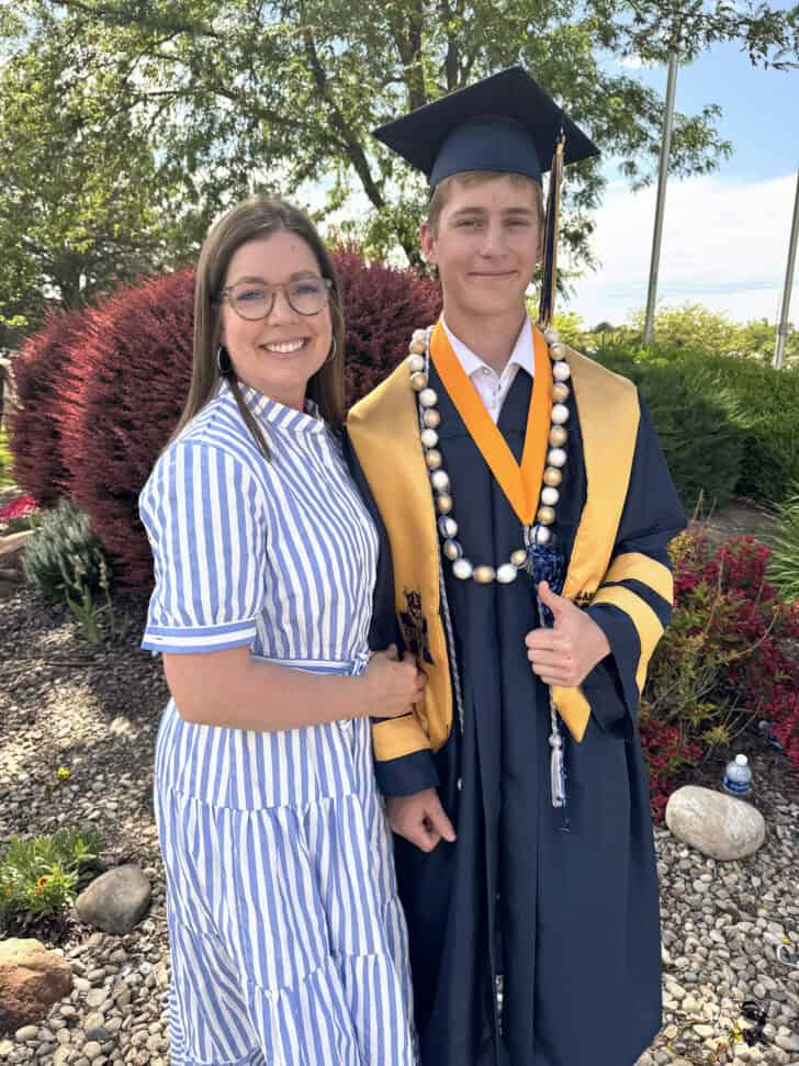 Mother and son standing together with son in graduation robe.
