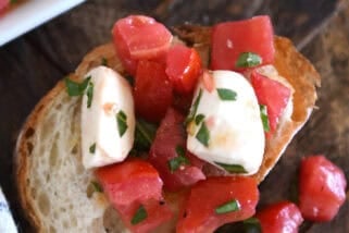 Top down view of a baguette slice with a tomato and mozzarella salad on top of the bread and spilling off the sides.