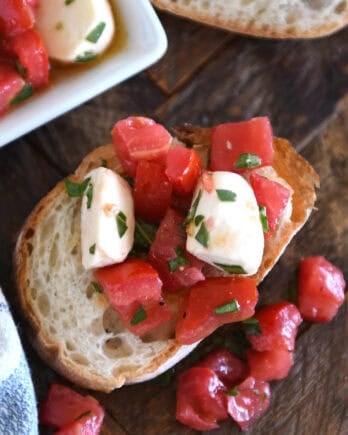 Top down view of a baguette slice with a tomato and mozzarella salad on top of the bread and spilling off the sides.