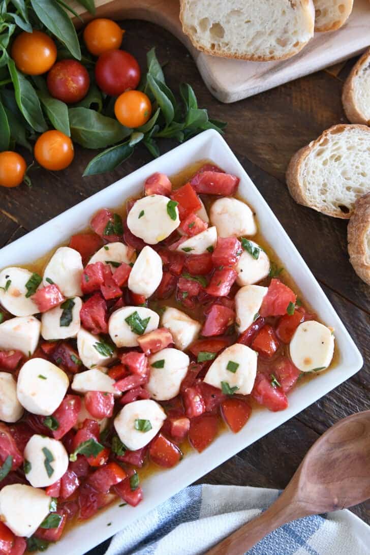 Top down view of a a white dish full of tomato mozzarella caprese salad.