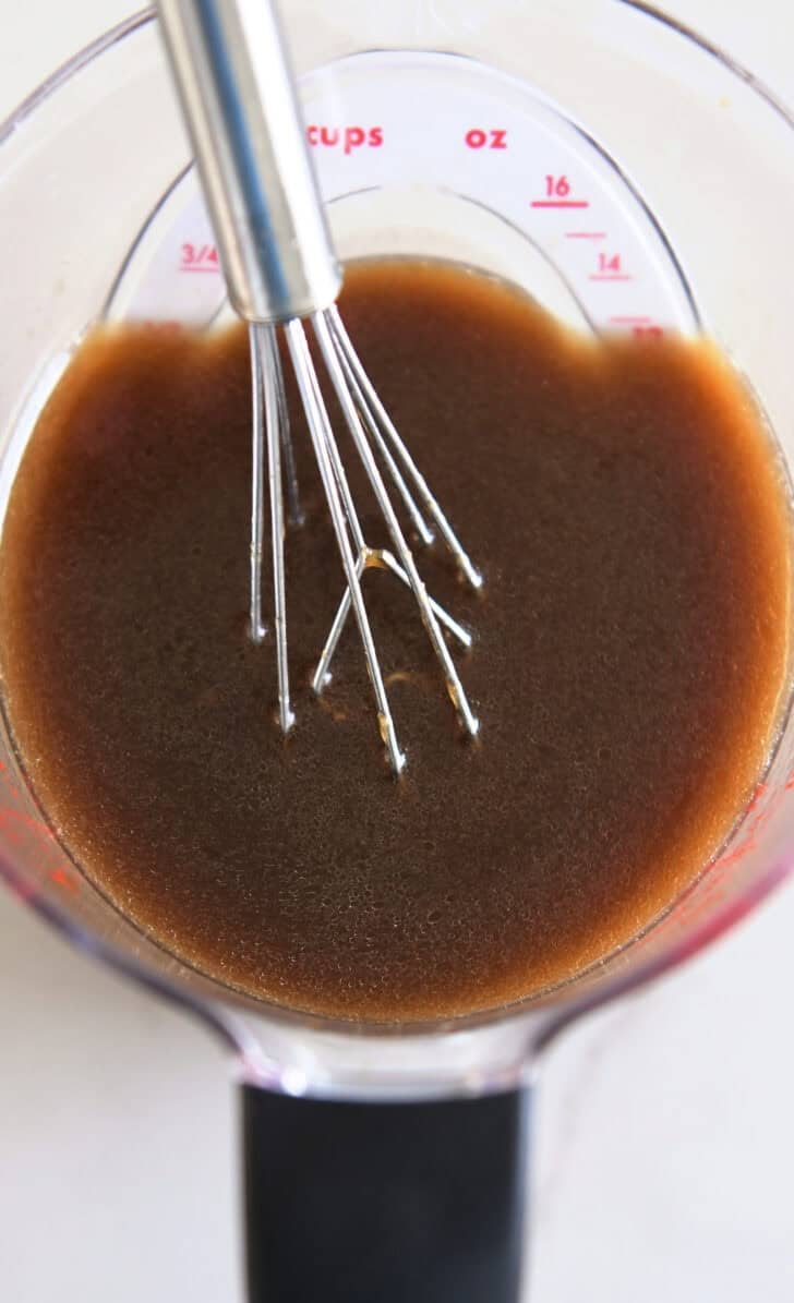 Liquid measuring cup with small whisk and Asian-style dressing.