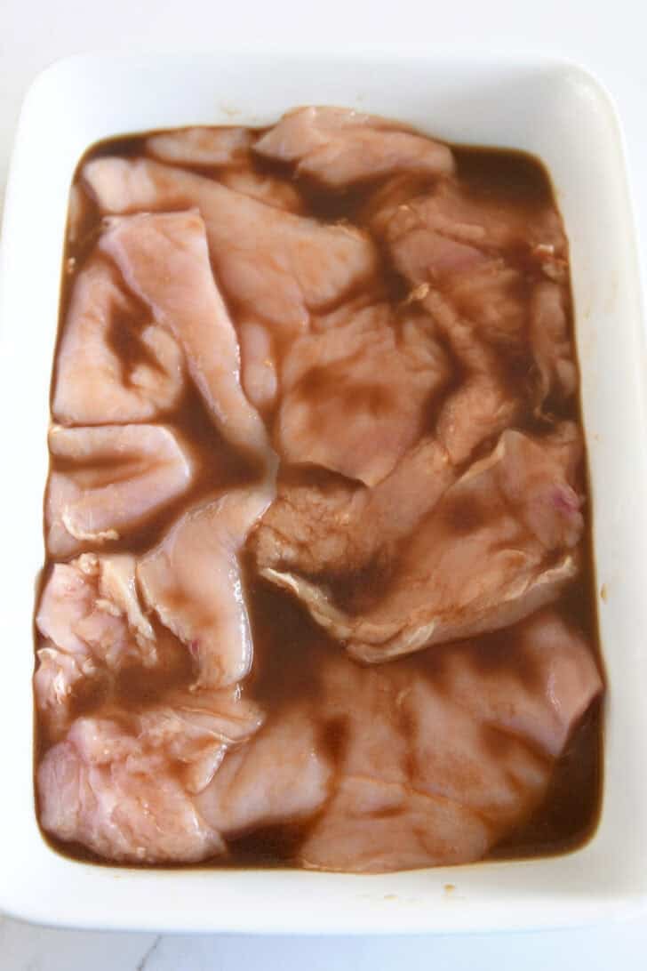 White pan with thinly sliced chicken breasts and Asian-style marinade.