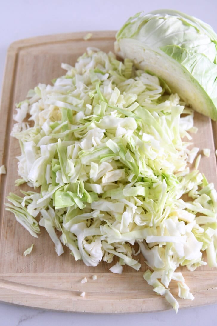 Chopped green cabbage on wood cutting board.