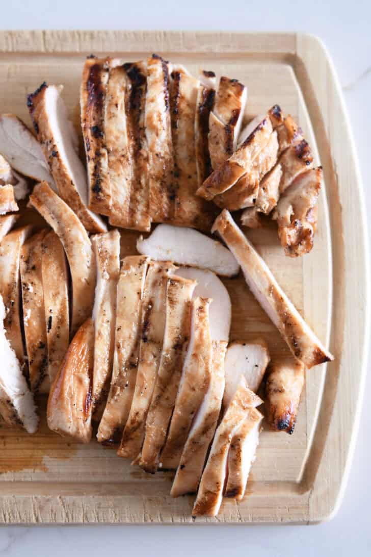 Thinly sliced grilled chicken on wood cutting board.