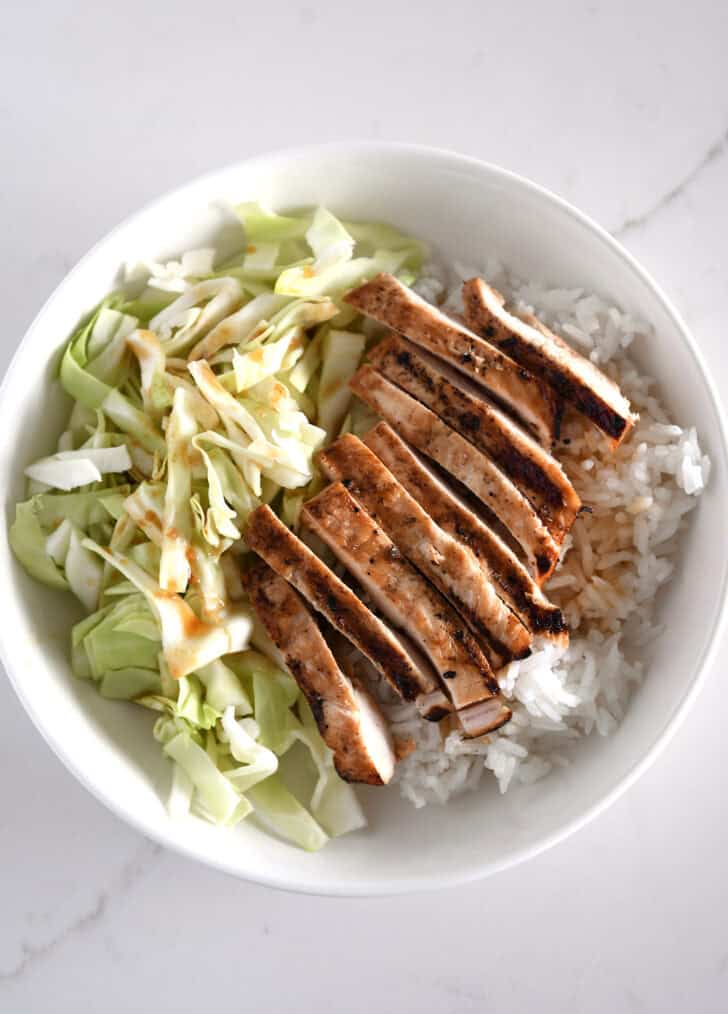 White bowl with chopped cabbage, white rice and grilled chicken.