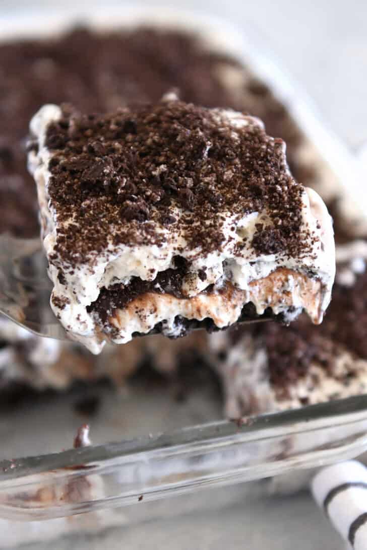 Square of Oreo ice cream dessert on spatula over glass 9X13-inch pan.