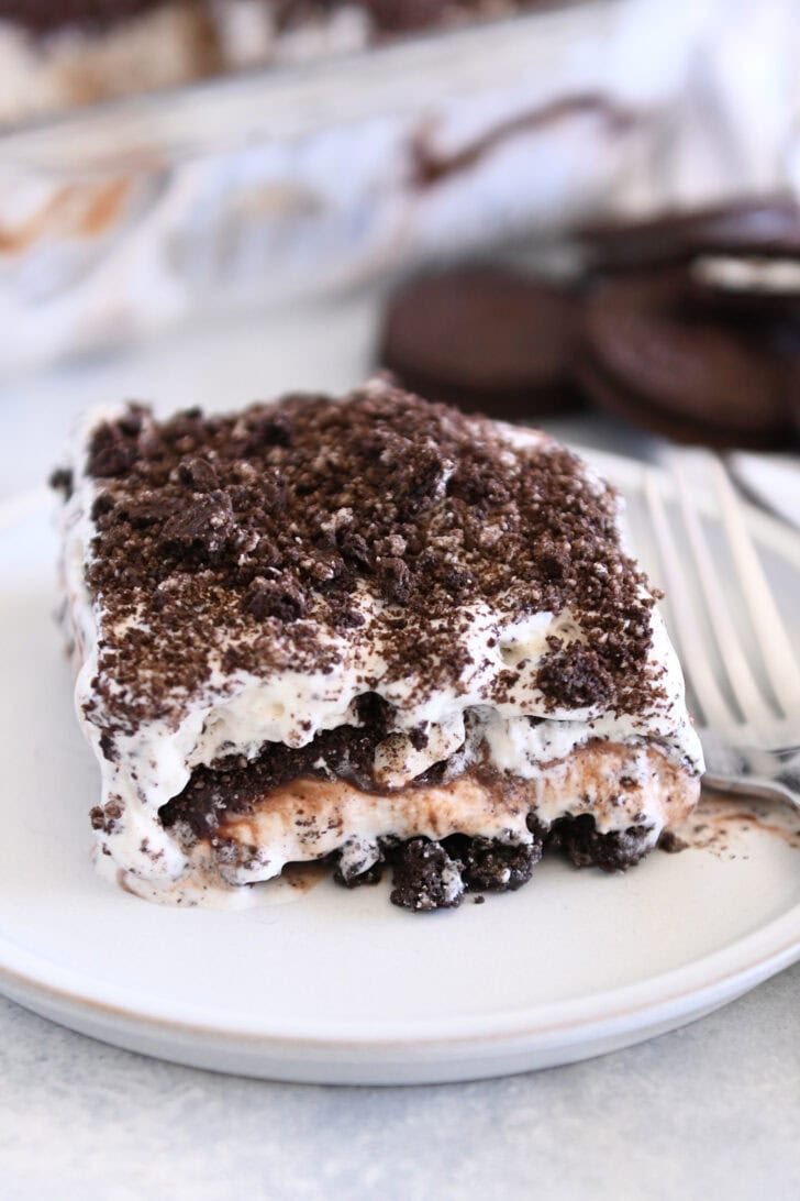 Square of layered Oreo ice cream dessert on gray plate with fork.