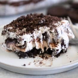 Square of layered Oreo ice cream dessert on gray plate with bite taken out.
