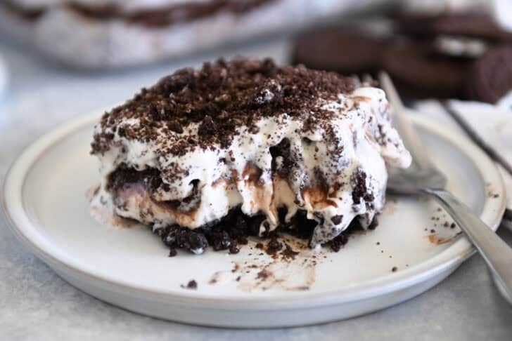 Square of layered Oreo ice cream dessert on gray plate with bite taken out.