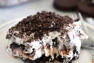 Square of layered Oreo ice cream dessert on gray plate with bite taken out.