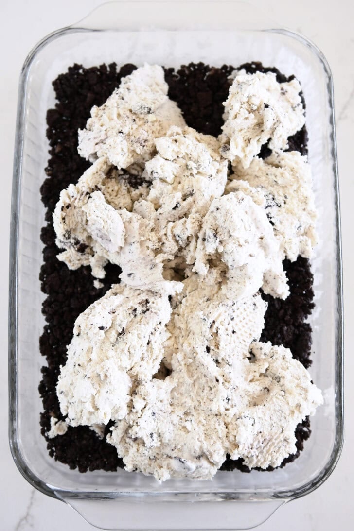 Piles of cookies and cream ice cream over Oreo crust in glass 9X13-inch pan.