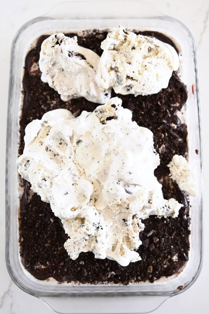 Piles of cookies and cream ice cream on top of crushed Oreos in glass 9X13-inch pan.