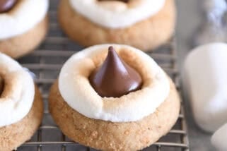 Assembled s'mores blossom cookies with toasted marshmallows and Hershey's Kisses on cooling rack.