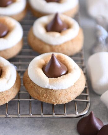 Assembled s'mores blossom cookies with toasted marshmallows and Hershey's Kisses on cooling rack.
