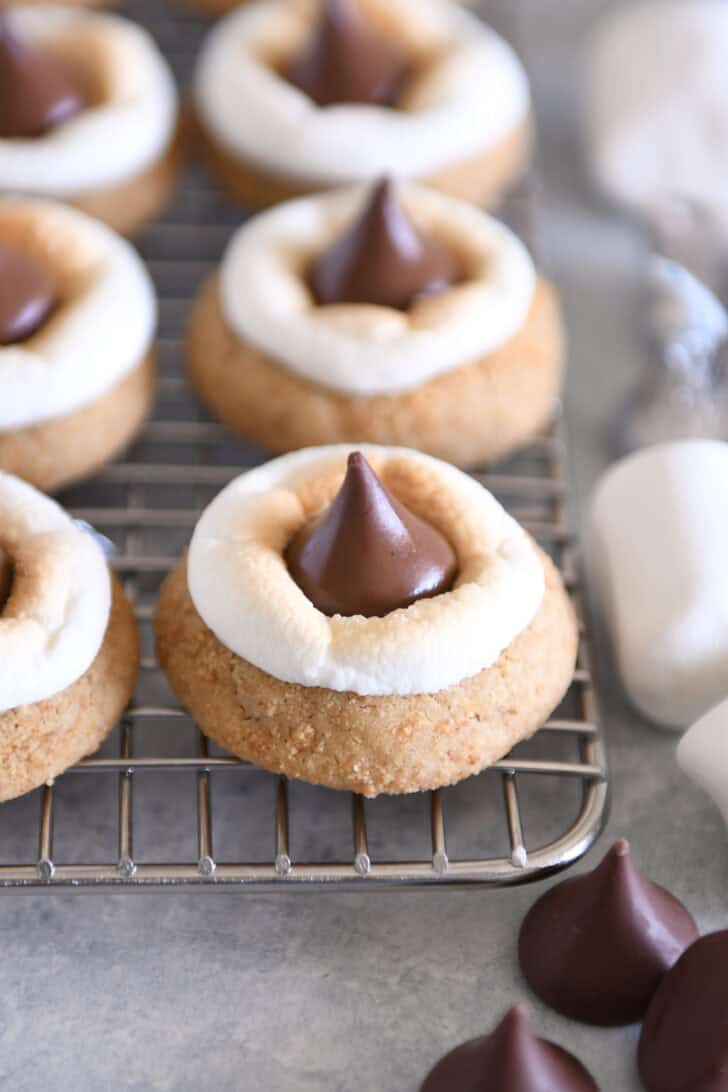 Assembled s'mores blossom cookies with toasted marshmallows and Hershey's Kisses on cooling rack.