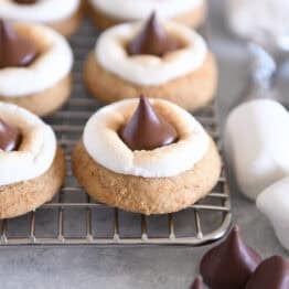 Assembled s'mores blossom cookies with toasted marshmallows and Hershey's Kisses on cooling rack.