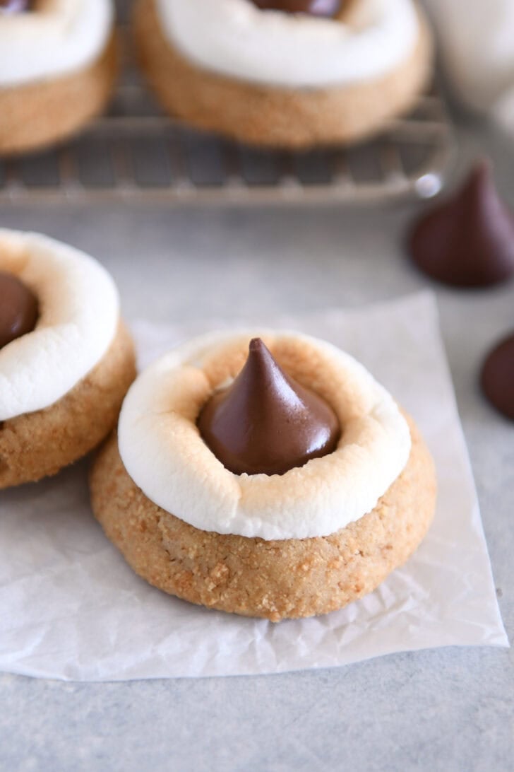 Graham cracker cookie with toasted marshmallow and Hershey's Kiss on white parchment paper.