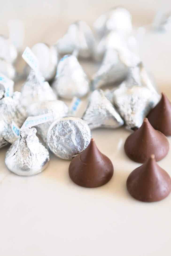 Wrapped silver Hershey's Kisses next to several unwrapped milk chocolate Hershey's Kisses.