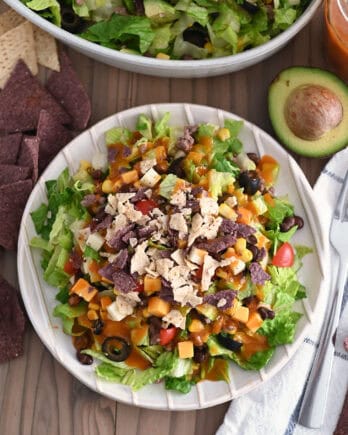 Top down view of White ridged plate with chopped taco salad and drizzled with homemade catalina dressing.