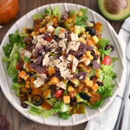 Top down view of White ridged plate with chopped taco salad and drizzled with homemade catalina dressing.