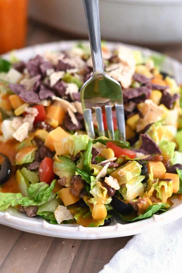 Fork scooping bite of chopped taco salad on white ridged plate.