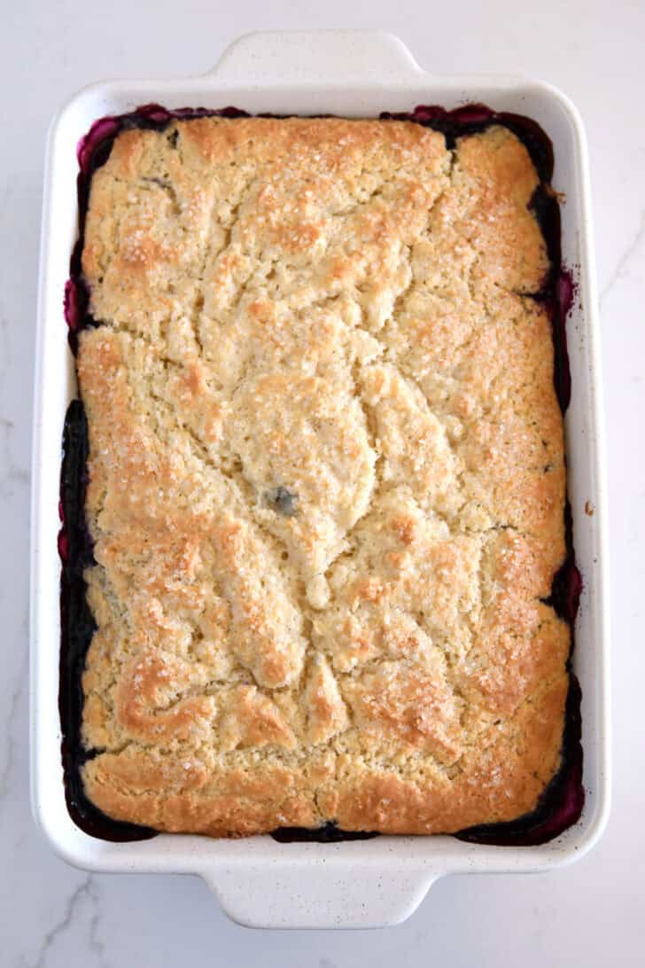 Baked triple berry cobbler with golden cobbler topping in white pan.