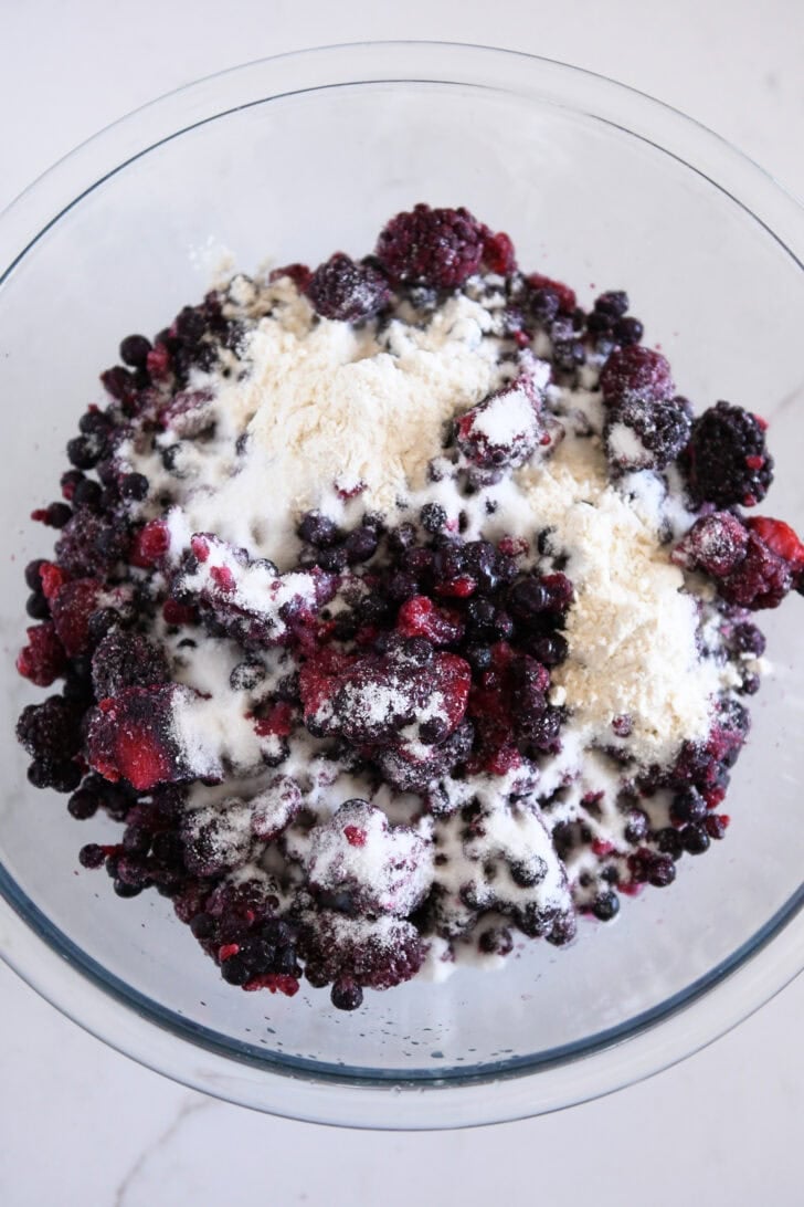 Raspberries, bluberries and blackberries in glass bowl with flour and sugar.