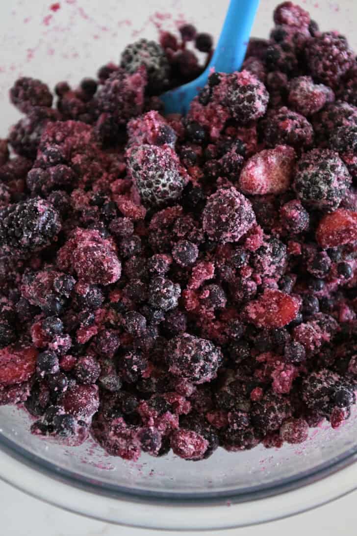 Triple berry mixture mixed with sugar and flour in glass bowl.