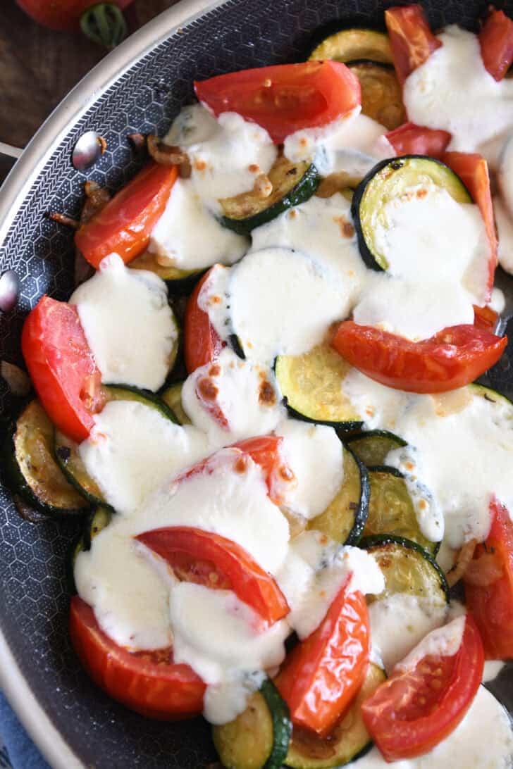 Top down view of a skillet full of sautéed vegetables and melted mozzarella cheese.