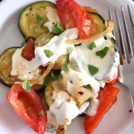 Top down view of a white plate with sautéed zucchini, onions, and tomatoes with melted mozzarella covering the top.