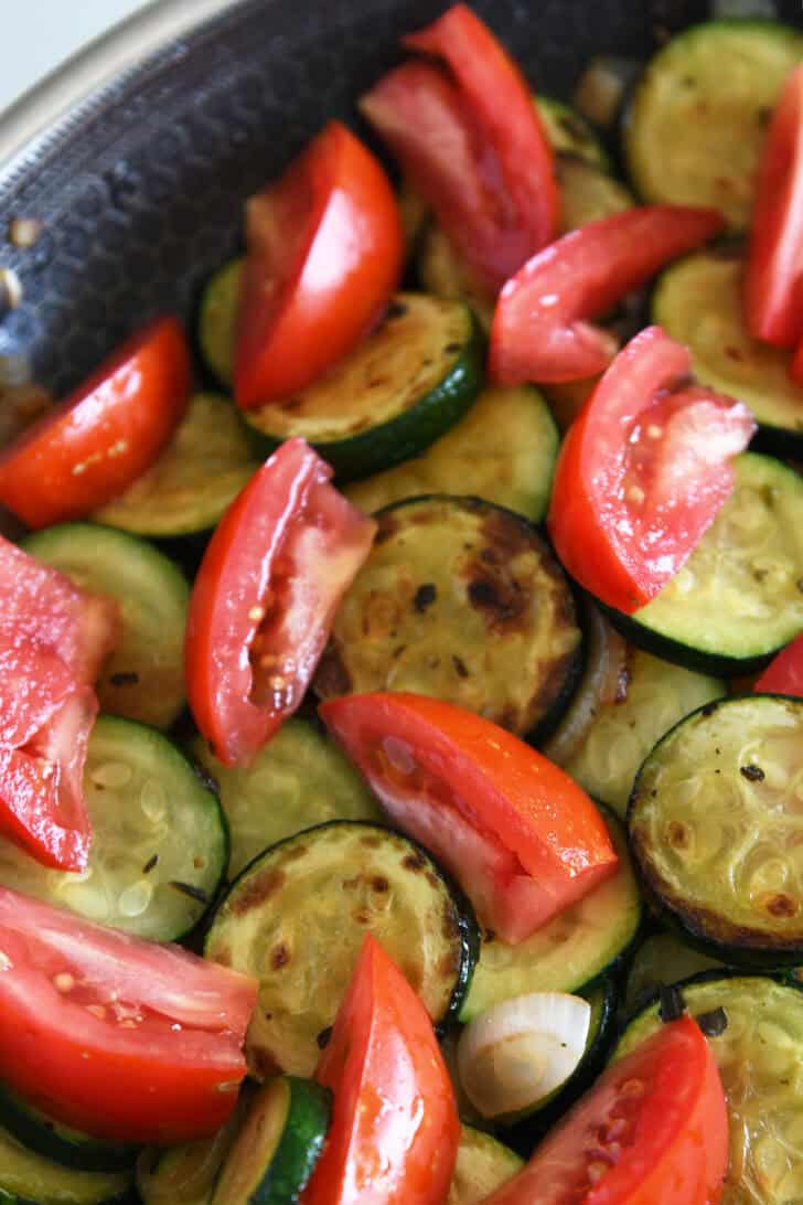Top down view of a skillet full of sautéed zucchini, tomatoes, and onions.