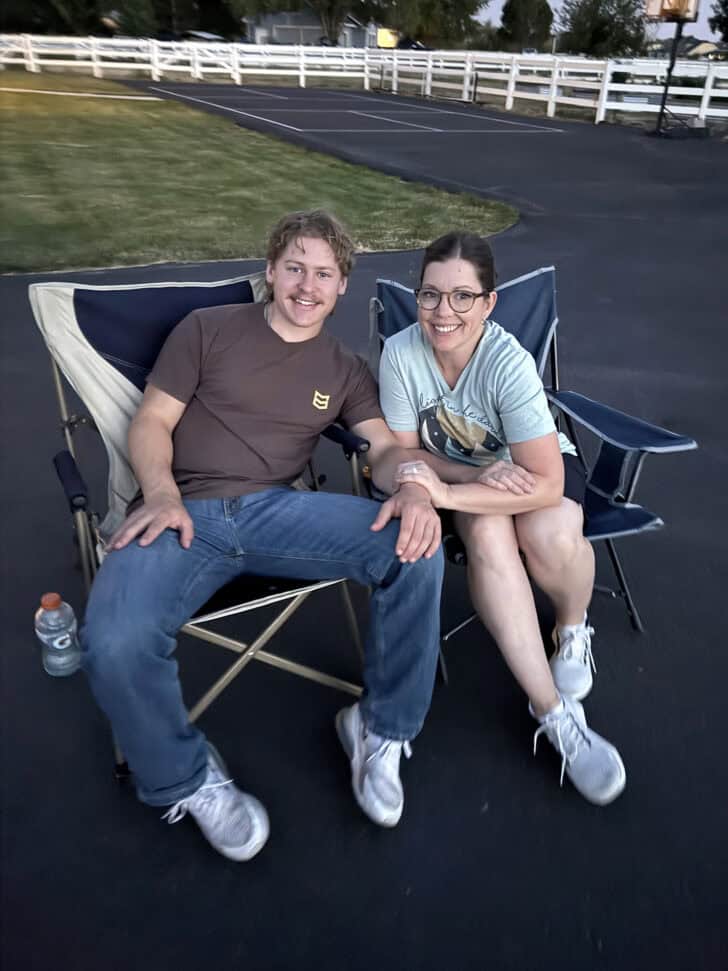 Mom sitting by adult son in camping chairs.