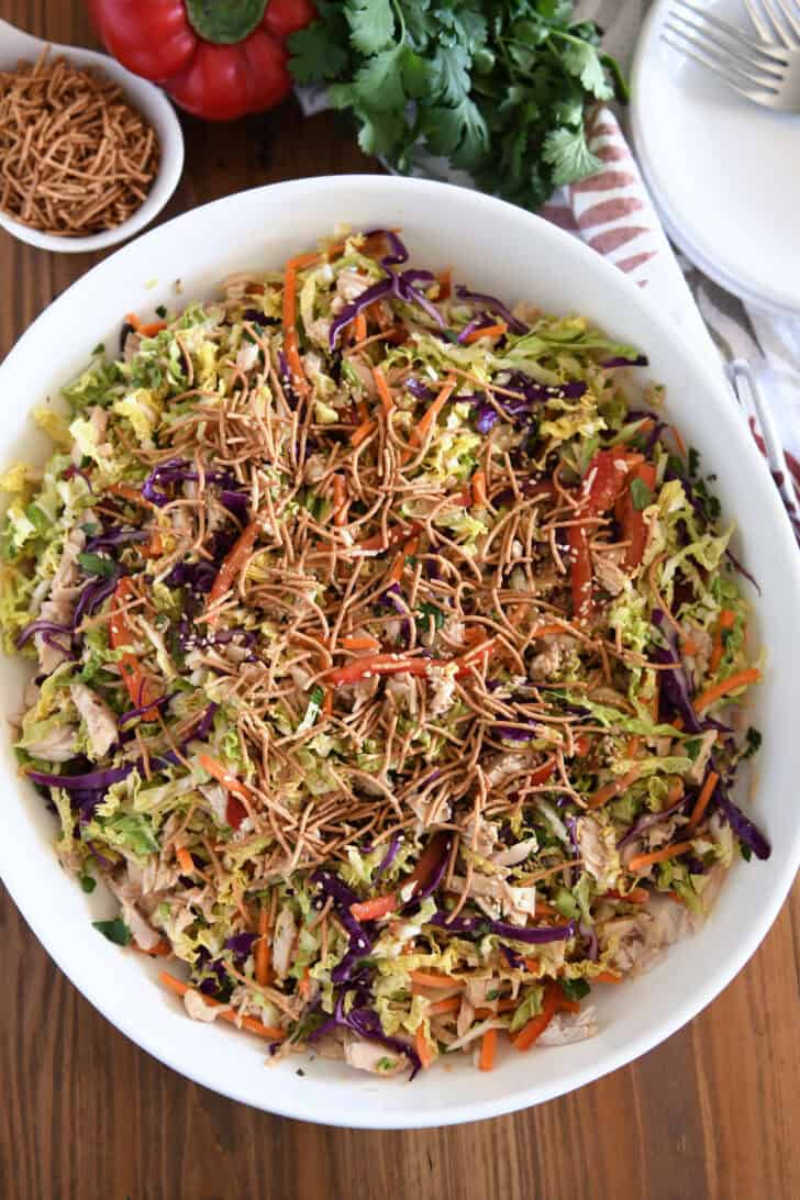 Asian chicken salad topped with chow mein noodles in white bowl.