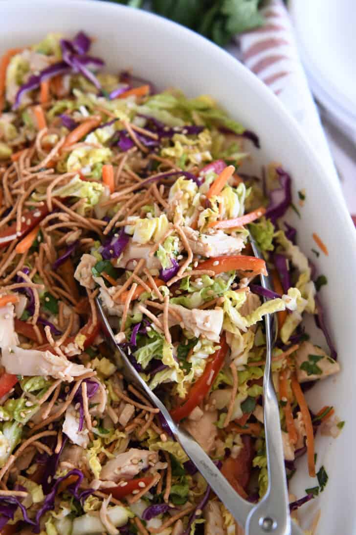 Salad tongs in bowl with Asian chicken salad ingredients.