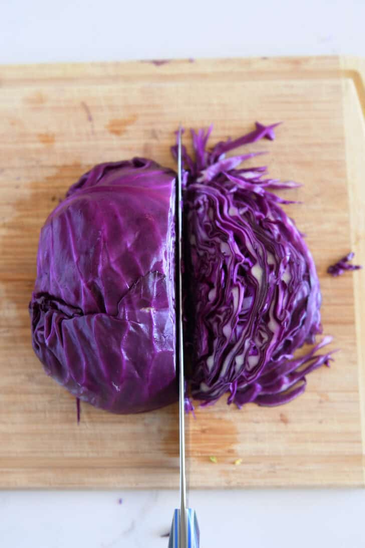 Thinly slicing red cabbage on wood cutting board.