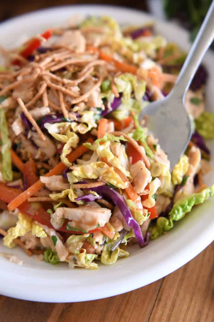 Fork scooping up Asian chicken salad on white plate.