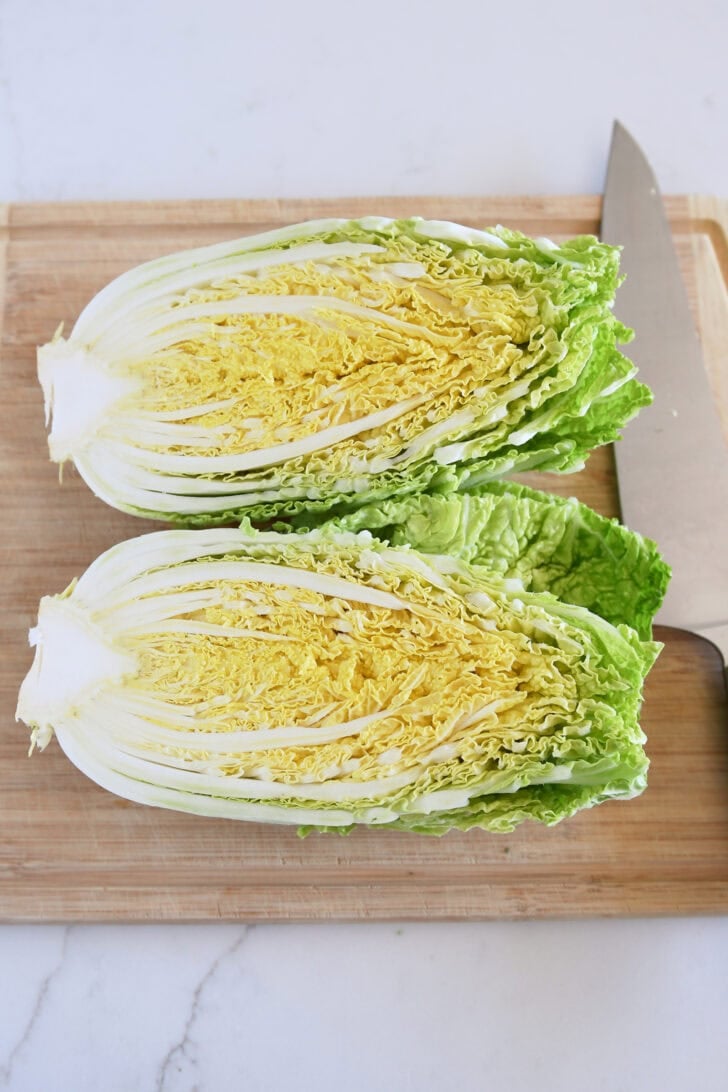 Napa cabbage cut in half on wood cutting board.