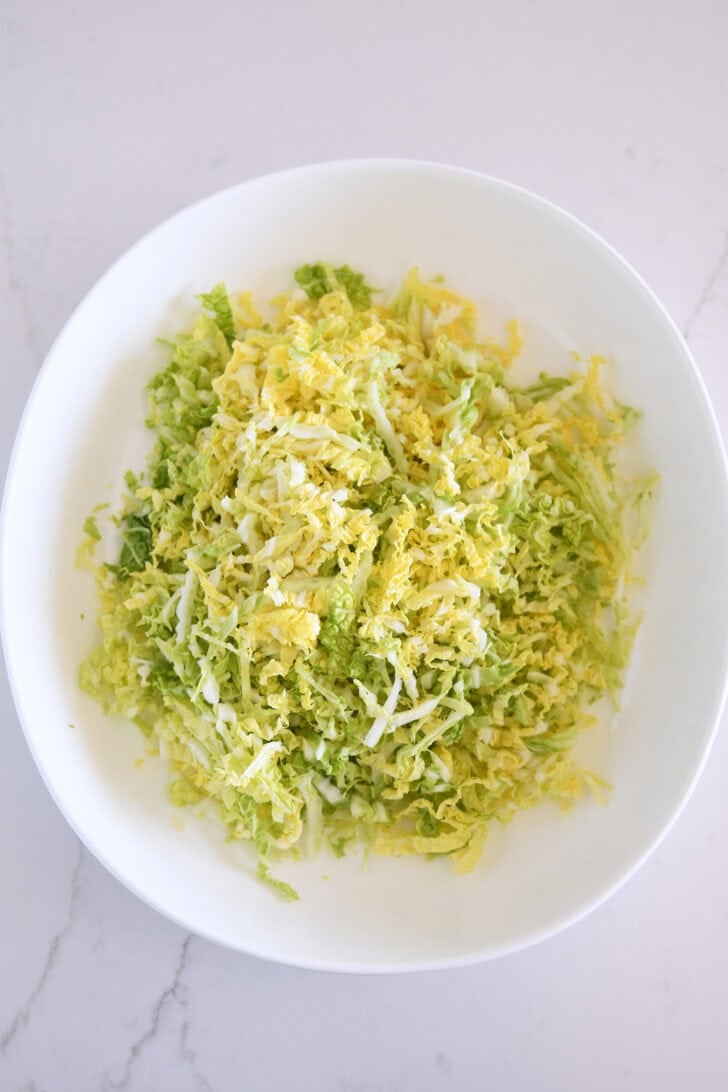 Napa cabbage thinly sliced in white bowl.