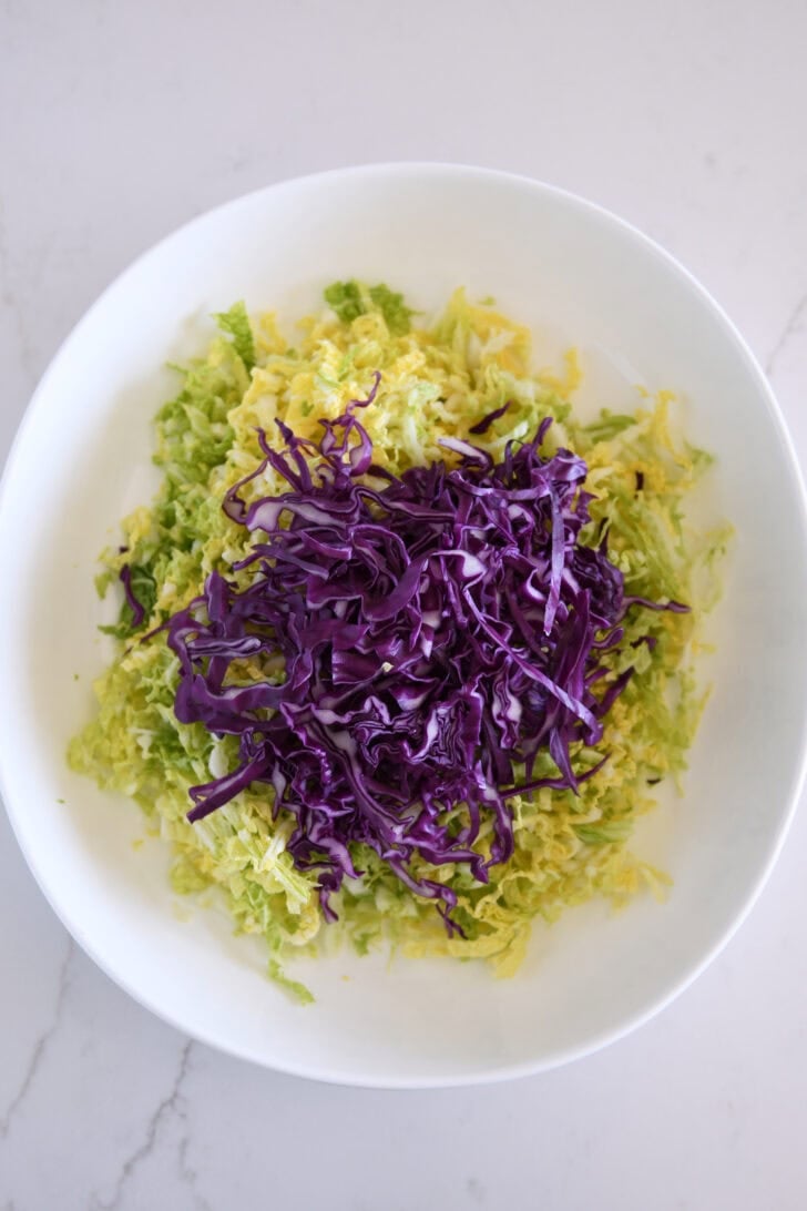 Thinly sliced red cabbage in bowl with thinly sliced napa cabbage.