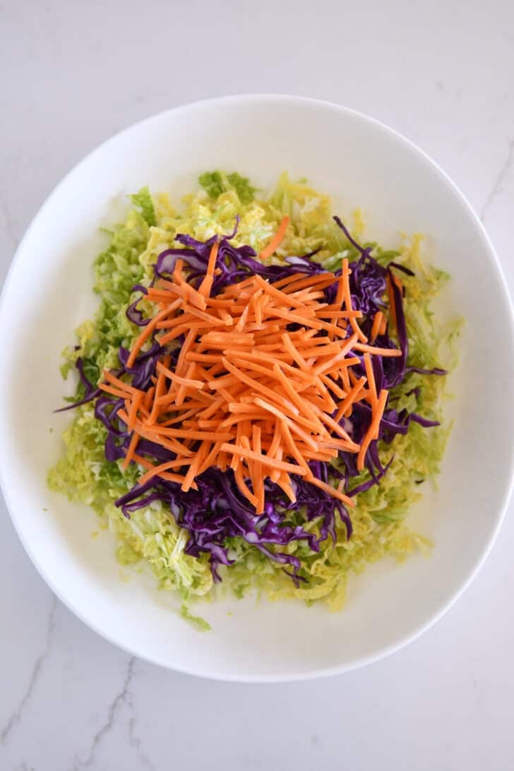 Thinly chopped carrots in bowl with red and Napa cabbage.